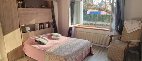 Un dormitorio con una cama de madera, un ventanal con vistas, un radiador y una silla.