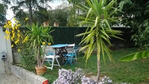 A garden with a variety of plants and flowers, a concrete border, and a table with chairs.