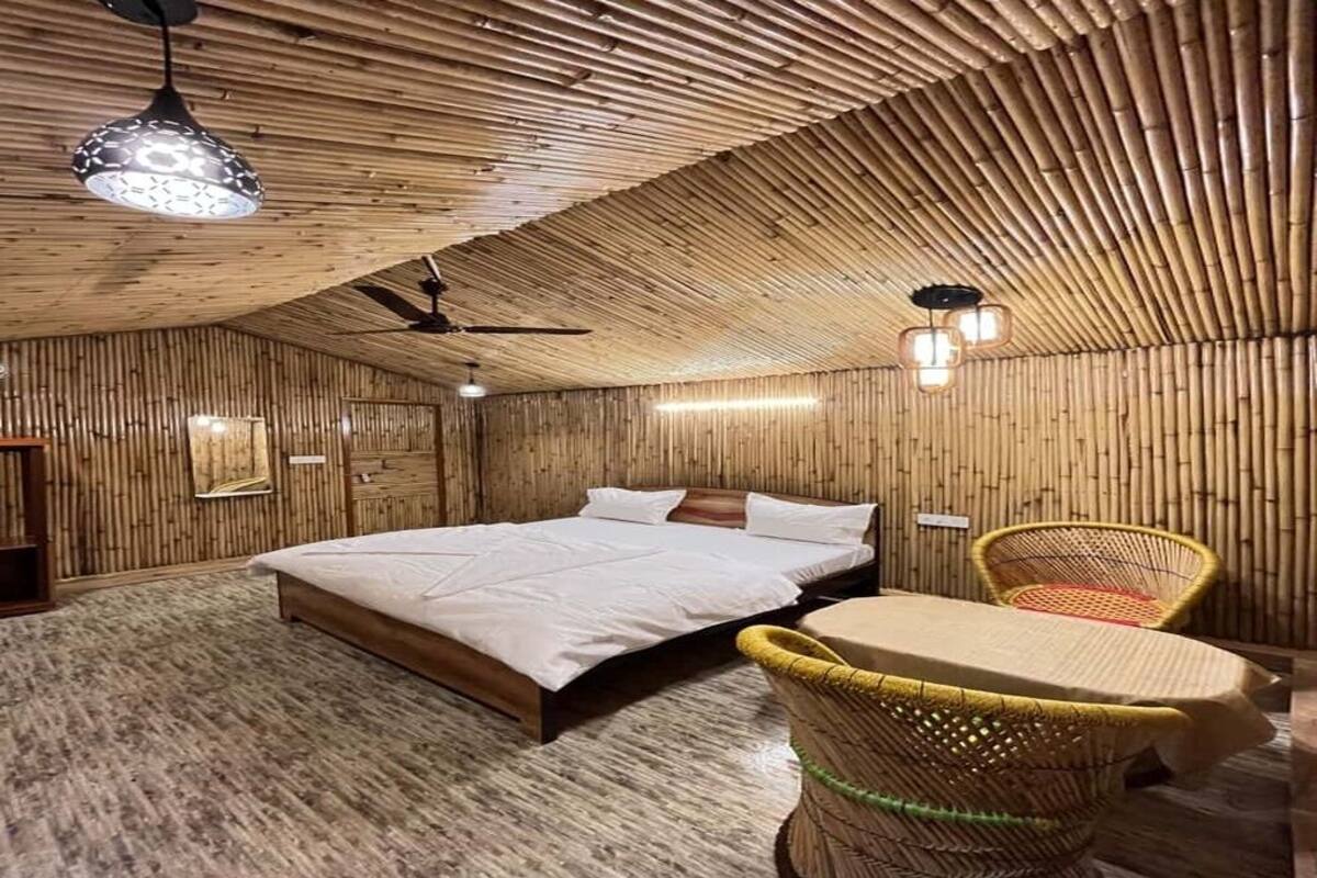 A room with a sloped ceiling, a bed, a table, wicker chairs, and wall-mounted lights.