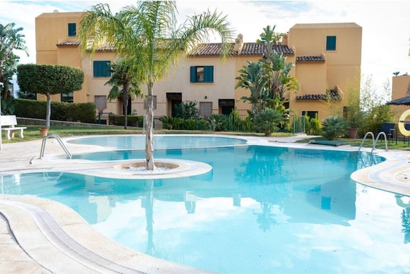 A swimming pool with a circular design, surrounded by palm trees and a building with a tiled roof. - PINAR vacation home  (Finestrat)