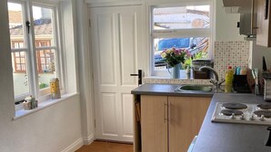 A modern kitchen with a built-in stove, a sink, and a window overlooking a street. - Central Bridport, a cosy pet-friendly cottage. (Bridport)