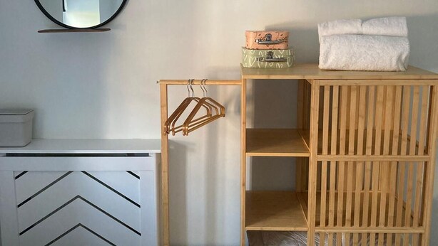 A room with a white dresser, a wooden crib with a hanging organizer, and a round mirror on the wall. - Central Bridport, a cosy pet-friendly cottage. (Bridport)