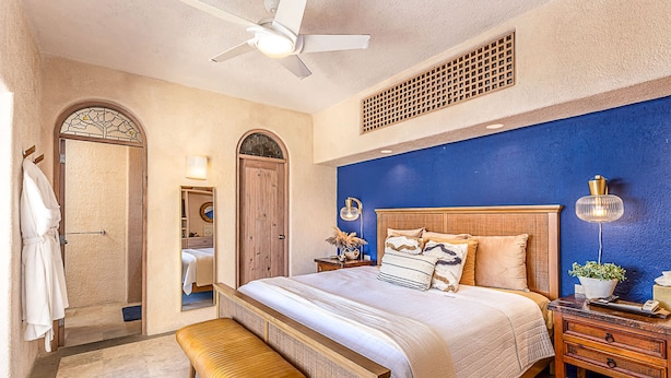 A bedroom with a large bed, a bench, a ceiling fan, and a nightstand with a lamp. - w Chic 5BR Oceanview Villa w Pool in Pedregal (Cabo San Lucas)