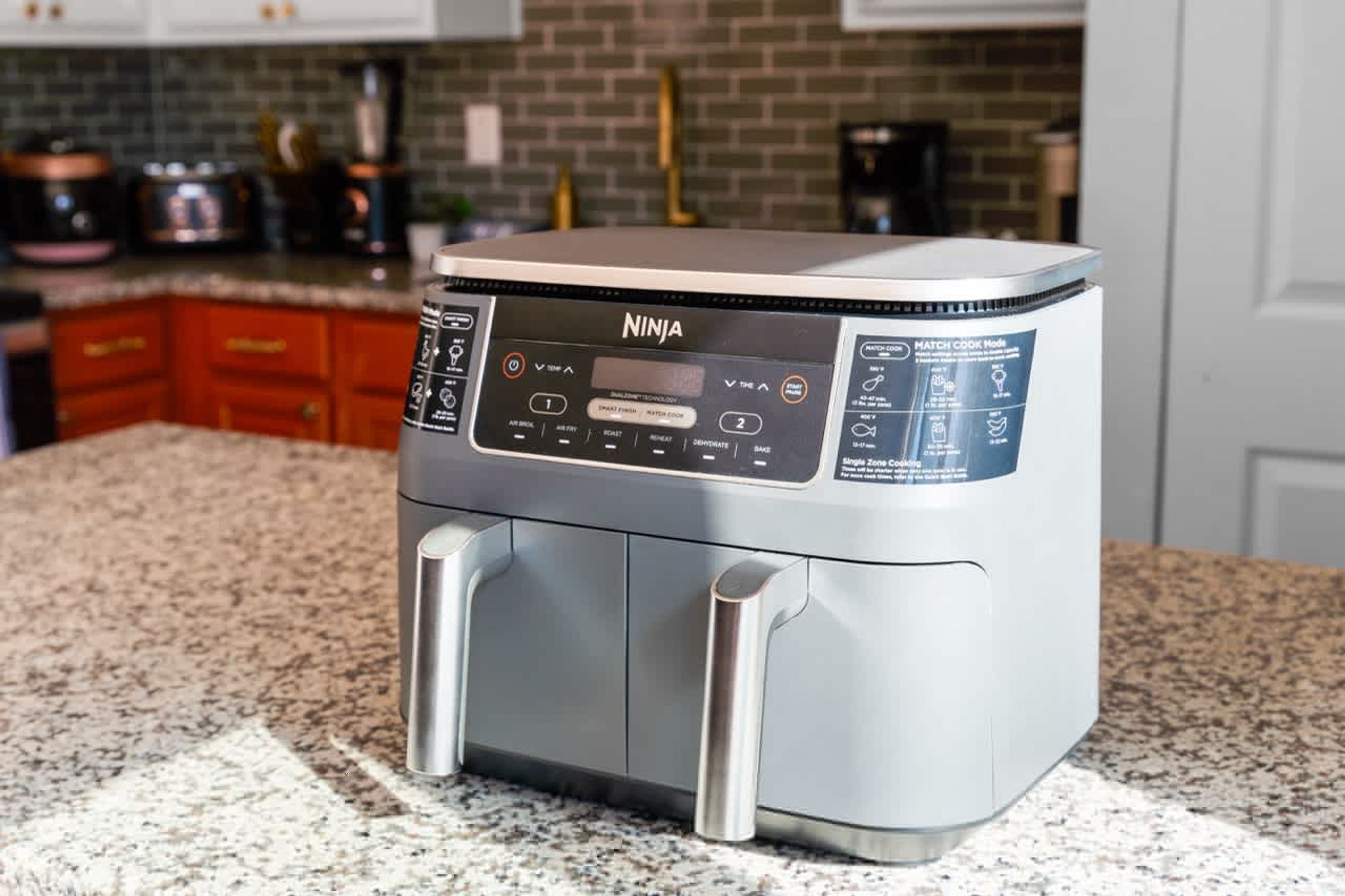 A Ninja air fryer on a kitchen counter with a granite countertop and red cabinets in the background.