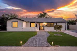A modern two-story house with a brick pathway leading to the entrance, surrounded by well-maintained lawns and a tree. - Chic Home With Backyard Oasis Pool Game Room (Phoenix)