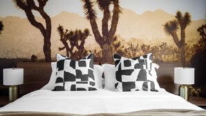 A bed with a desert-themed wall mural, two bedside lamps, and a woven blanket. - Chic Home With Backyard Oasis Pool Game Room (Phoenix)