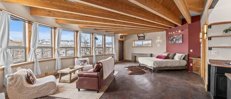A spacious living room with a high ceiling, large windows, and a fireplace.
