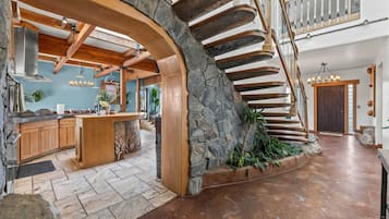 Una cocina amplia con una isla central, una pared de acento de piedra y una escalera de madera.