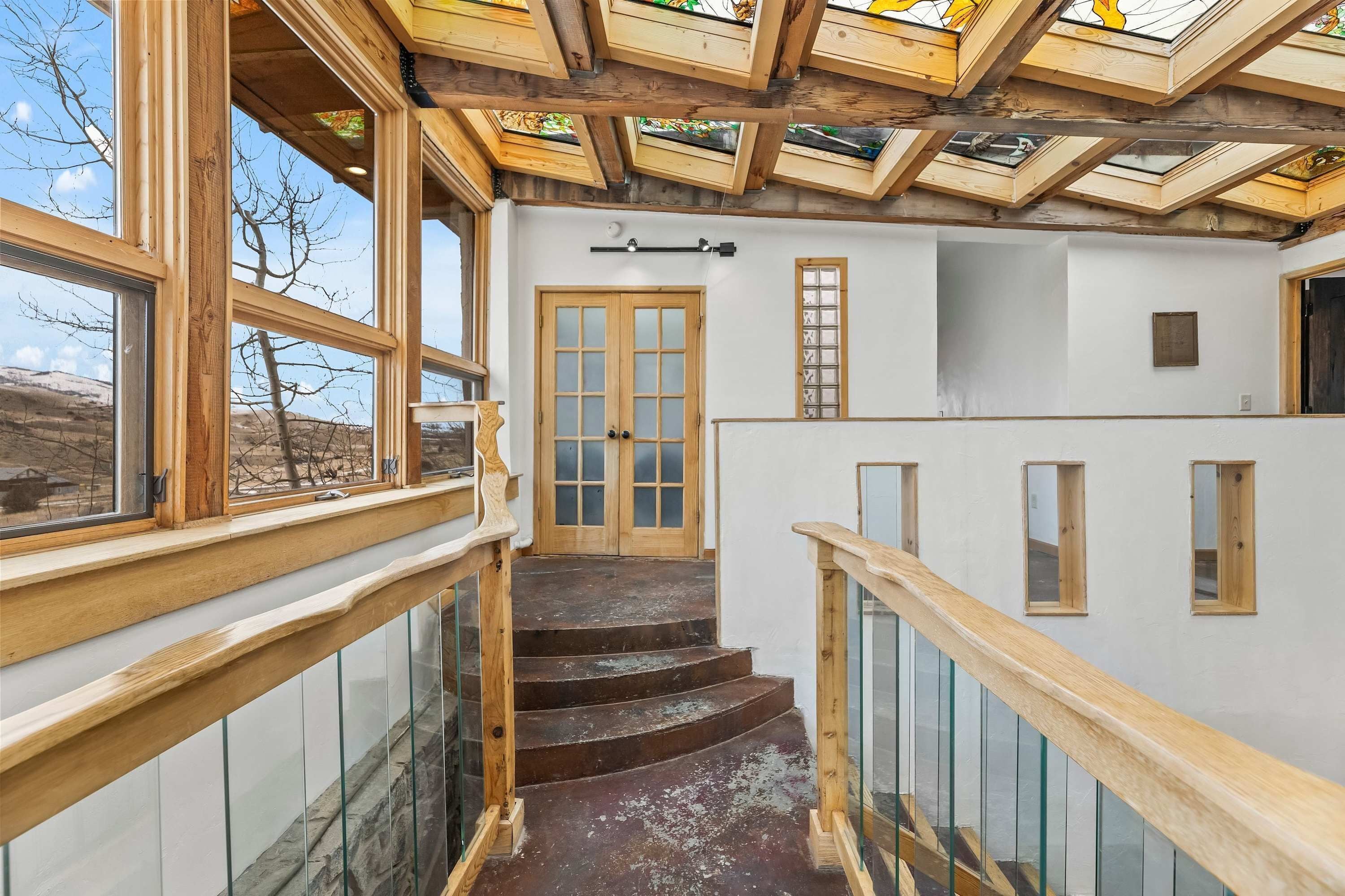 Un escalier avec des rampes en bois et des balustrades en verre, menant à une porte dotée de panneaux en verre dépoli.
