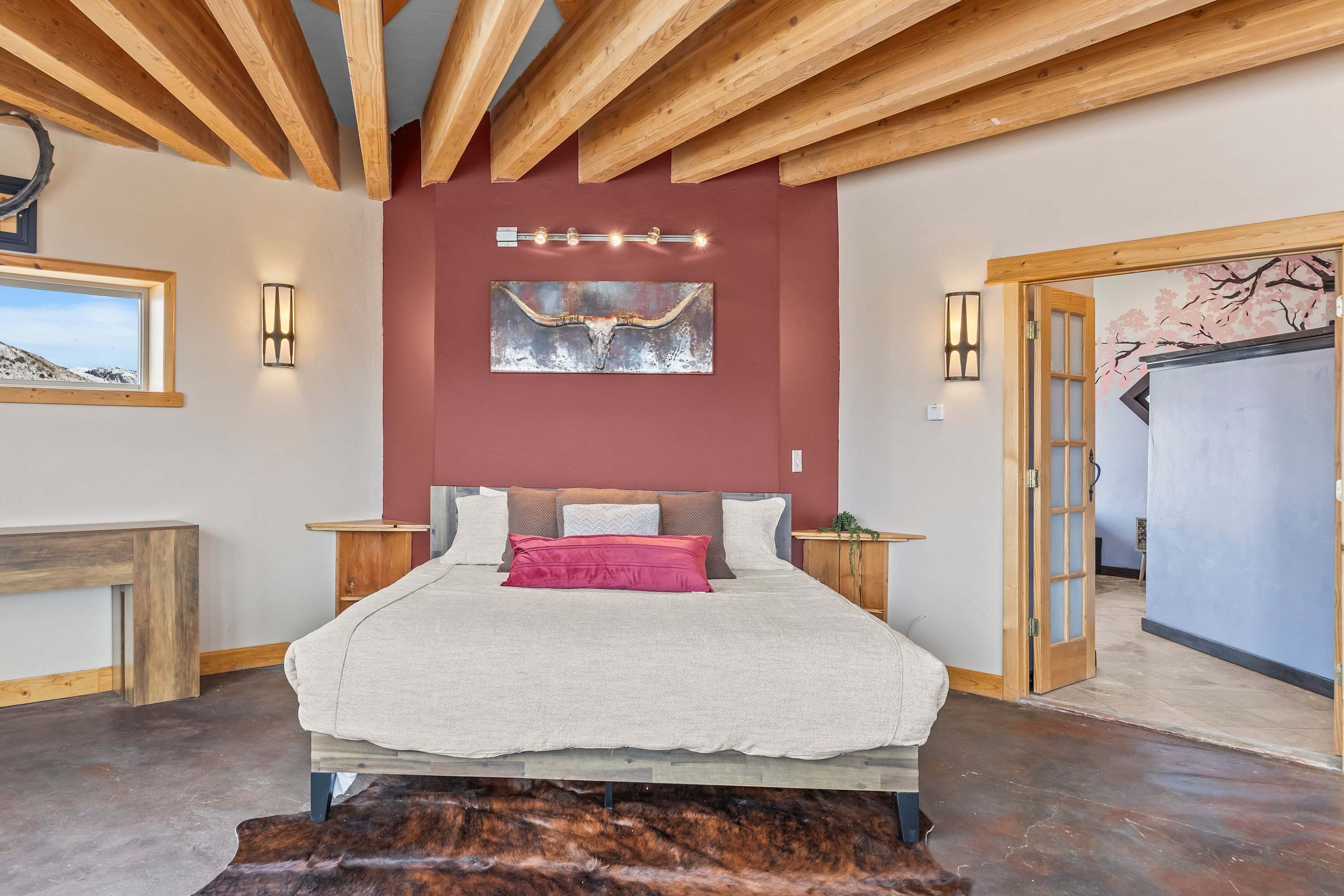 Ein Schlafzimmer mit einem Bett, Holzbalken, einer roten Akzentwand und Kunstwerken.