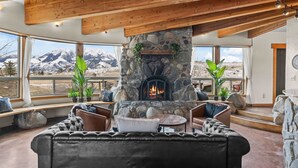 Ein gemütliches Interieur mit Kamin aus Stein, Ledersofas und großen Fenstern mit Blick auf die Berge.