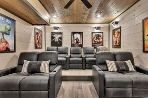 A home theater with six black leather recliner seats, wooden panel walls, and movie posters. - Firefly Lodge Indoor Pool Theater Hot Tub (Sevierville)