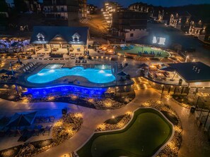 An aerial view of a resort with a large swimming pool, outdoor seating areas, and a golf course. - Firefly Lodge Indoor Pool Theater Hot Tub (Sevierville)
