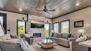 Una sala de estar moderna con chimenea de piedra, una mesa de centro de vidrio y un ventilador de techo.