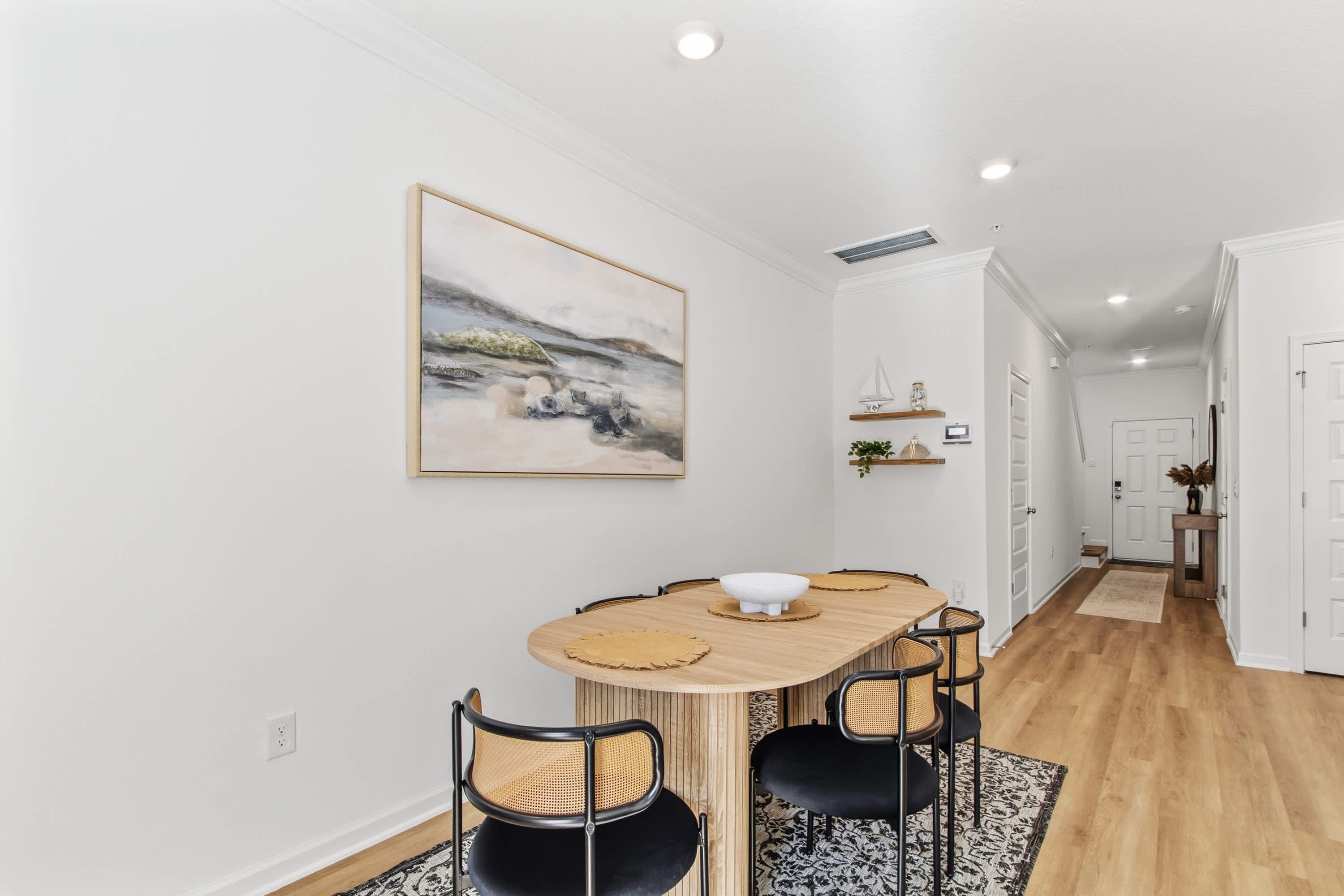 A dining area with a wooden table, black and wicker chairs, and a large landscape painting on the wall.
