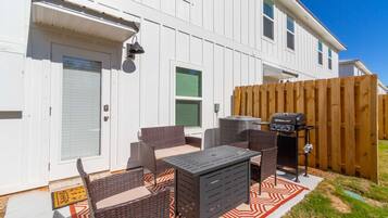 Un patio con mobiliario de mimbre, una parrilla y una puerta con ventanal.