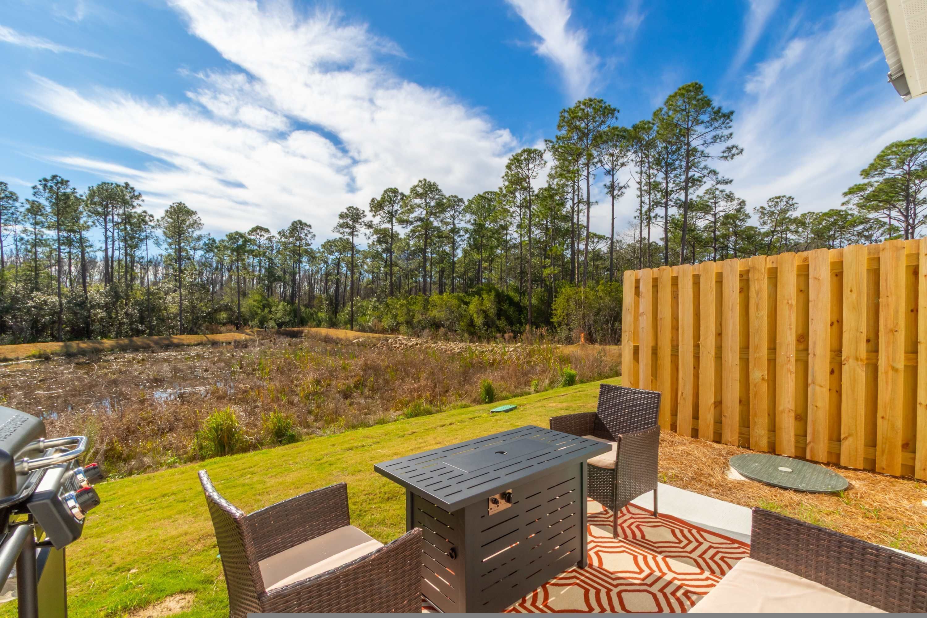 An outdoor patio with a grill, wicker furniture, and a view of a pond and forest.