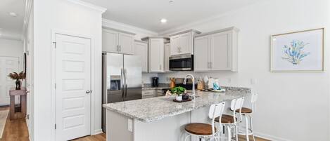 A modern kitchen with white cabinetry, a granite countertop, and a central island with bar stools.