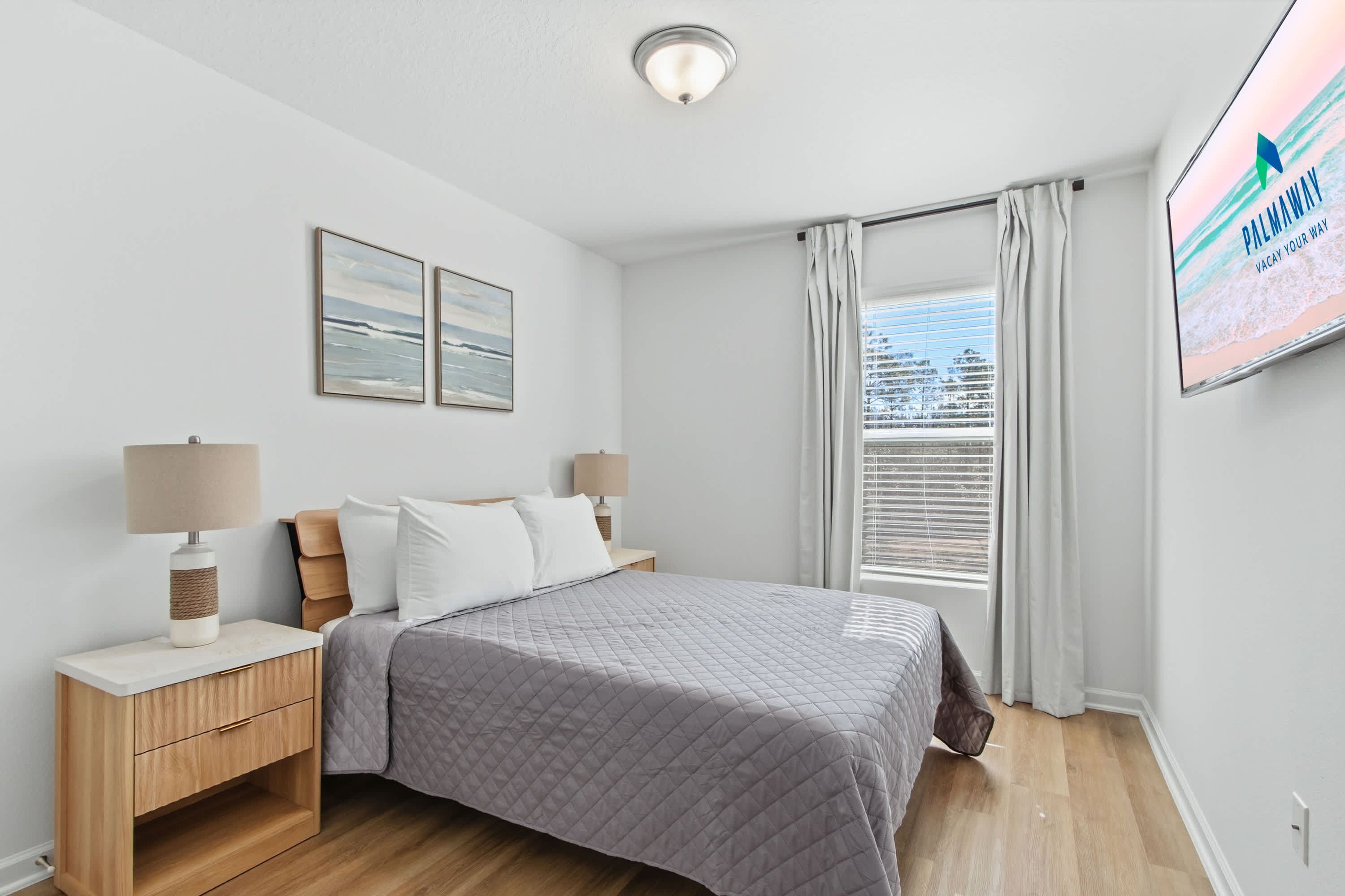 A bedroom with a bed, nightstands, a window with curtains, and wall art.
