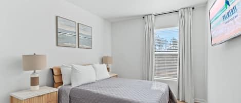 A bedroom with a bed, nightstands, a window with curtains, and wall art.