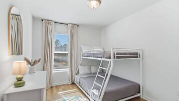 Ein Schlafraum mit Etagenbetten, Schreibtisch, Lampe und einem Fenster mit Vorhängen.