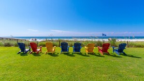 A row of colorful Adirondack chairs on a grassy lawn with a beach and ocean in the background. - NEW Sleeps 7 Beach Fun Dining Palmaway (Orange Beach)