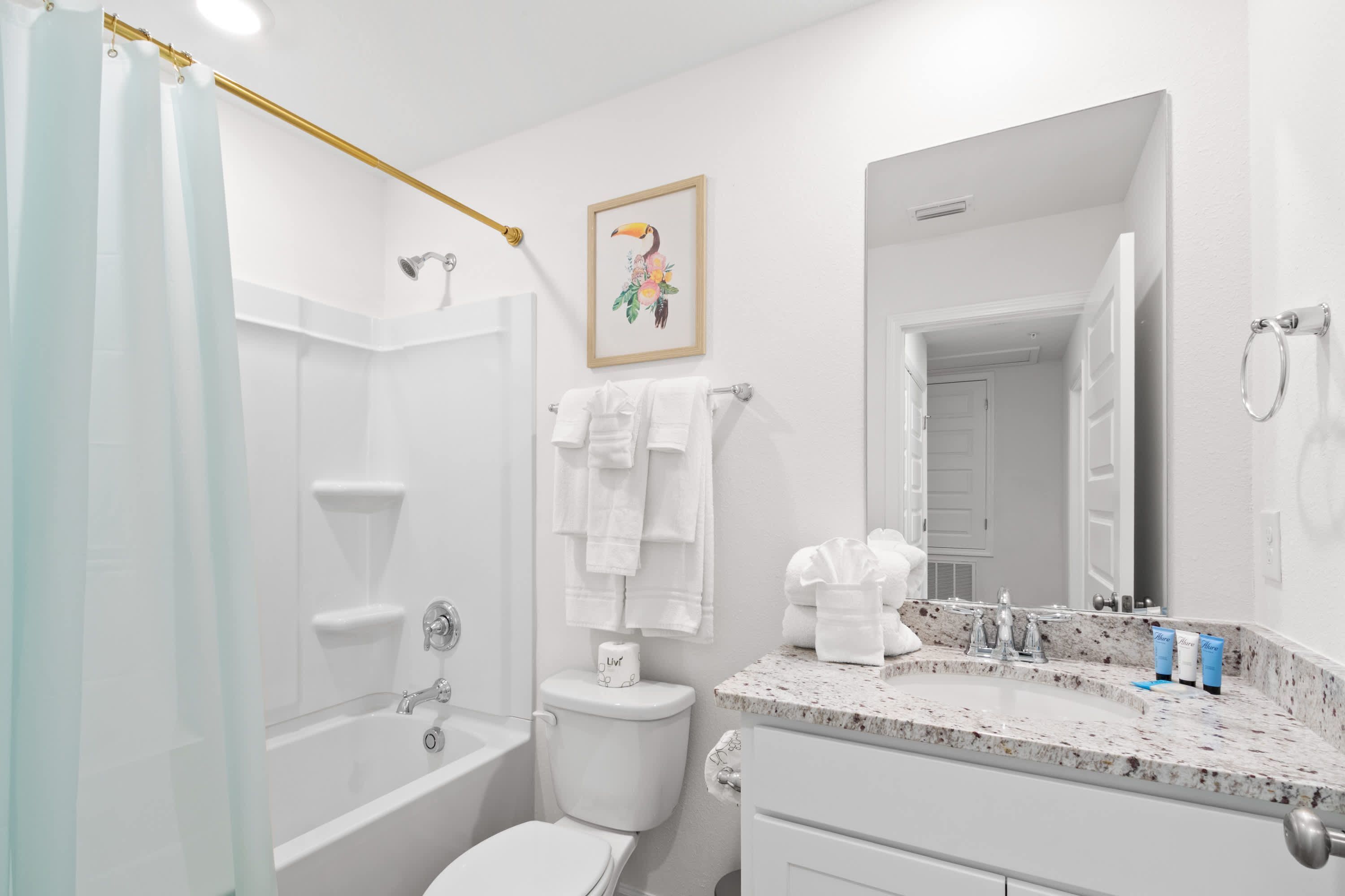 Une salle de bain moderne avec une baignoire, des toilettes et un lavabo. On y trouve un rideau de douche, un porte-serviettes et un tableau encadré au mur.
