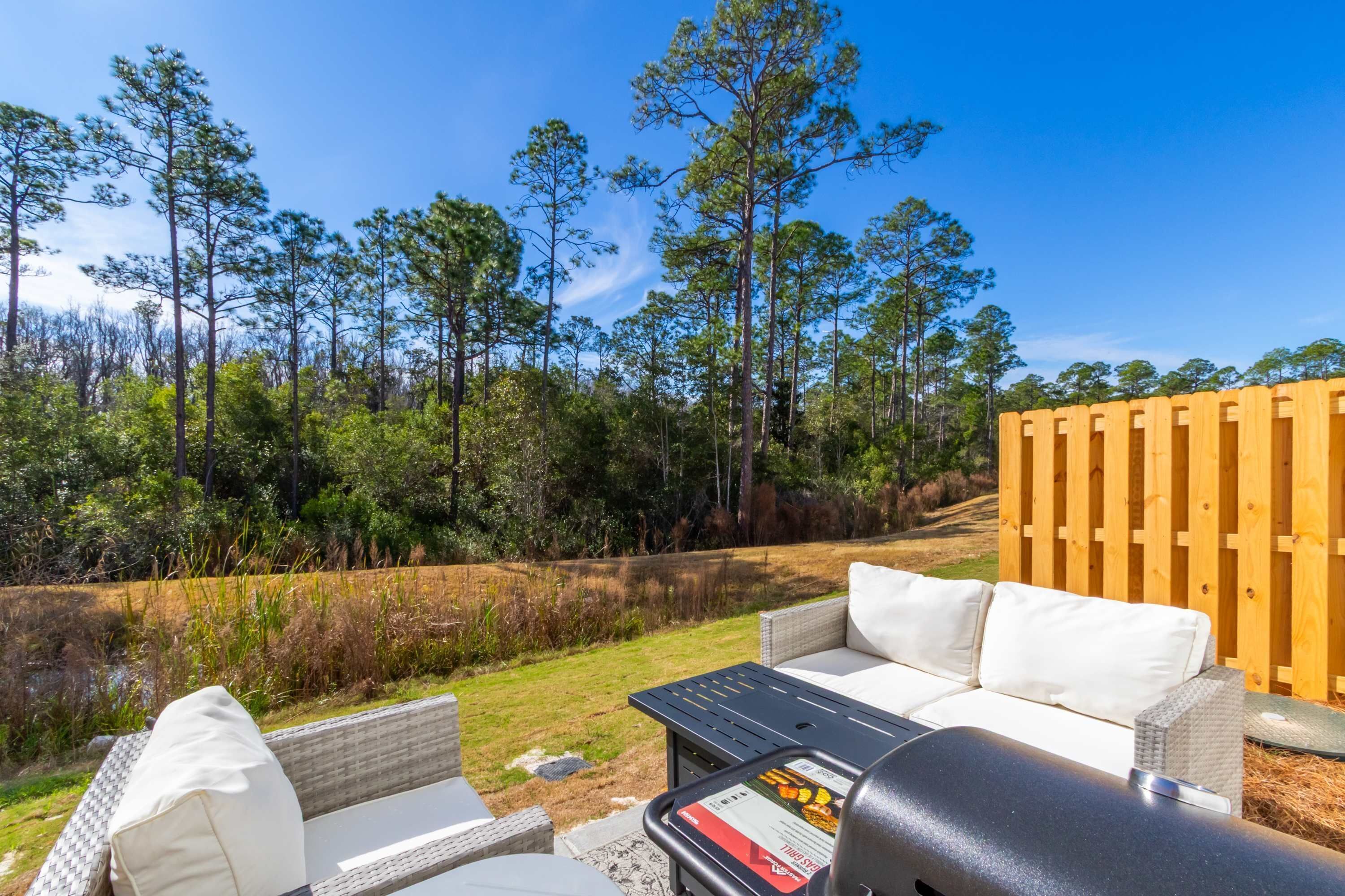 A patio with outdoor furniture, a grill, and a view of a forested area.