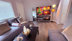 Ein modernes Wohnzimmer mit einer Couch, einem Couchtisch und einem Flachbildfernseher, der eine Weihnachtsszene zeigt.