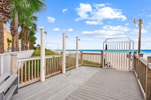 A wooden deck with a white railing, overlooking a beach with palm trees and a clear sky. - New UNIT, Penthouse with gulf views close to pier park! (Panama City Beach)