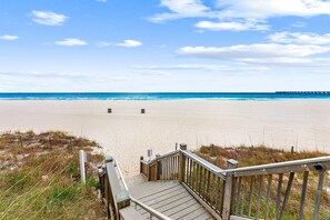A wooden staircase leading to a sandy beach with a clear sky and a distant pier. - New UNIT, Penthouse with gulf views close to pier park! (Panama City Beach)