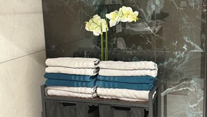 A bathroom with a black towel rack holding folded towels in white, blue, and beige. There is a vase with white flowers on the rack. - New house or town center + parking space (Dijon)