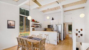 Una cocina moderna con armarios blancos, una isla central y un comedor con mesa y sillas de madera.