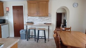 A compact kitchen with wooden cabinets, a tiled backsplash, and a dining area with a wooden table and chairs. - Portrush Country Cottage with sea views. Perfectly situated for sightseeing. (Coleraine)