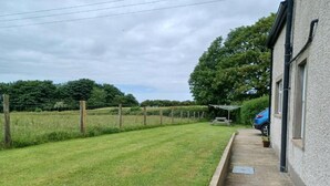 A grassy yard with a wooden fence, a picnic table, and a blue car parked beside a building. - Portrush Country Cottage with sea views. Perfectly situated for sightseeing. (Coleraine)