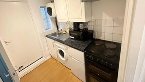 Ett kompakt kök med vita skåp, en tvättmaskin, en spis och en kaffebryggare.