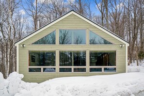 A two-story building with large windows and a gabled roof, surrounded by snow and trees. - 3 bedroom pet-friendly Killington retreat with fireplace and room for 8. (Killington)