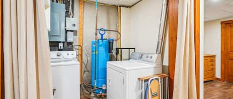 A laundry room with two washing machines, a blue water heater, and exposed electrical wiring.