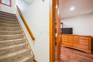 A staircase with carpeted steps and wooden handrails, leading to a room with a wooden cabinet and a television on a stand. - 3 bedroom pet-friendly Killington retreat with fireplace and room for 8. (Killington)