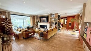 Ein geräumiges Wohnzimmer mit großem Fernseher, Holzboden und einer Sofagarnitur.