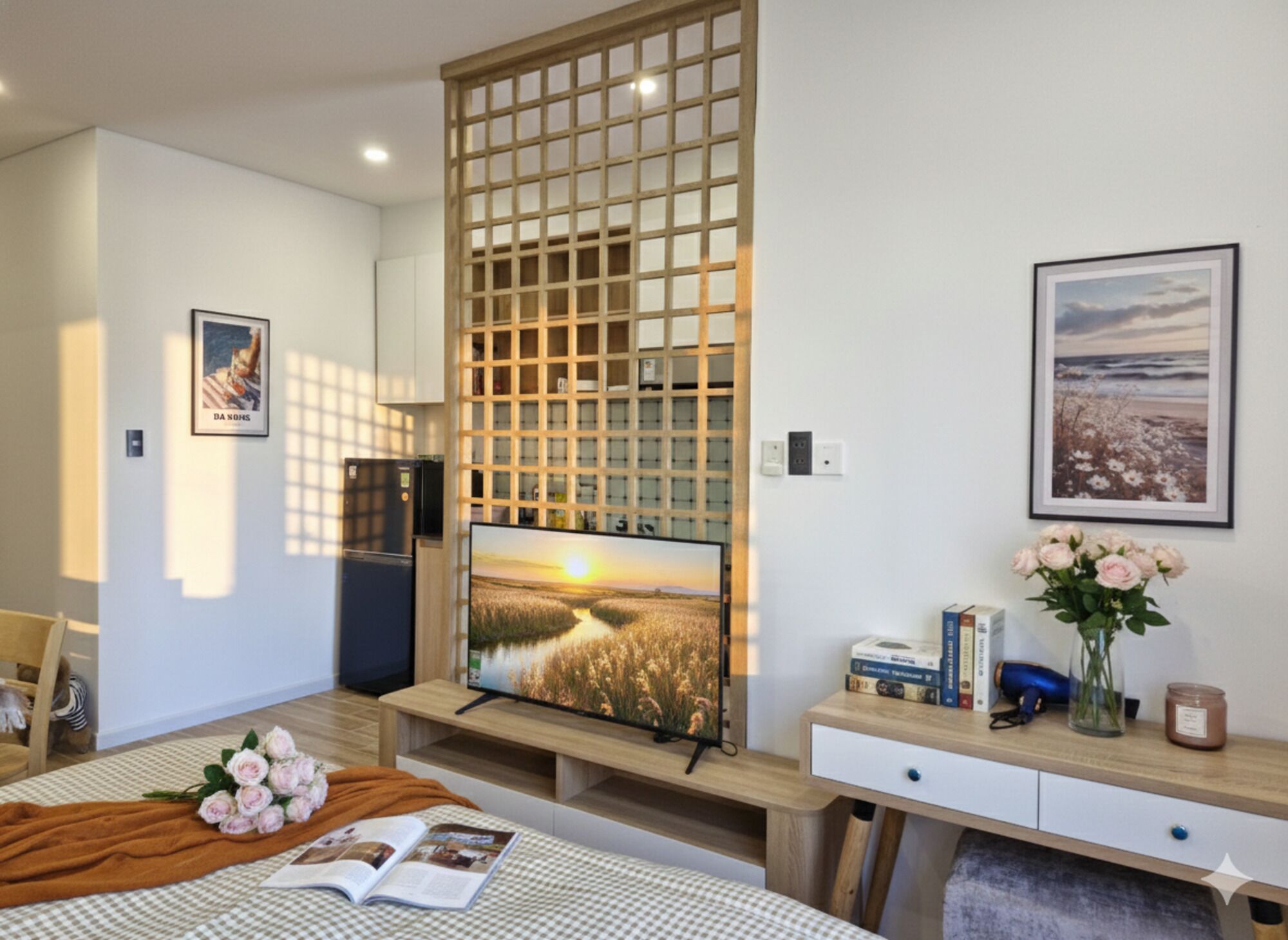 Une chambre moderne avec un téléviseur posé sur un meuble en bois, une bibliothèque, une table de chevet avec des livres et un vase de fleurs, et une fenêtre donnant sur un champ.