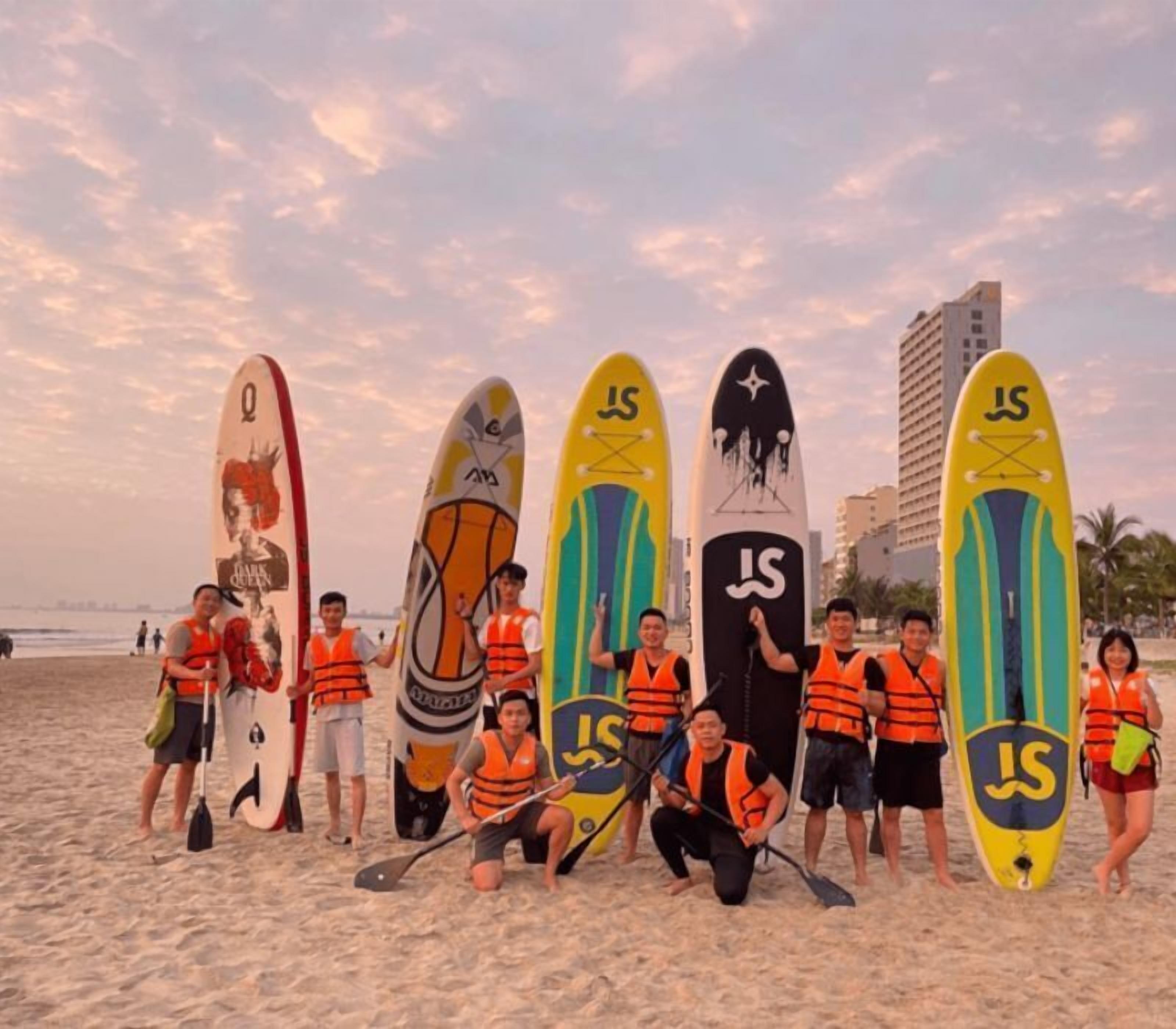 Un groupe de personnes se trouve sur une plage, tenant des planches de surf sur lesquelles on peut voir les lettres « JS ».