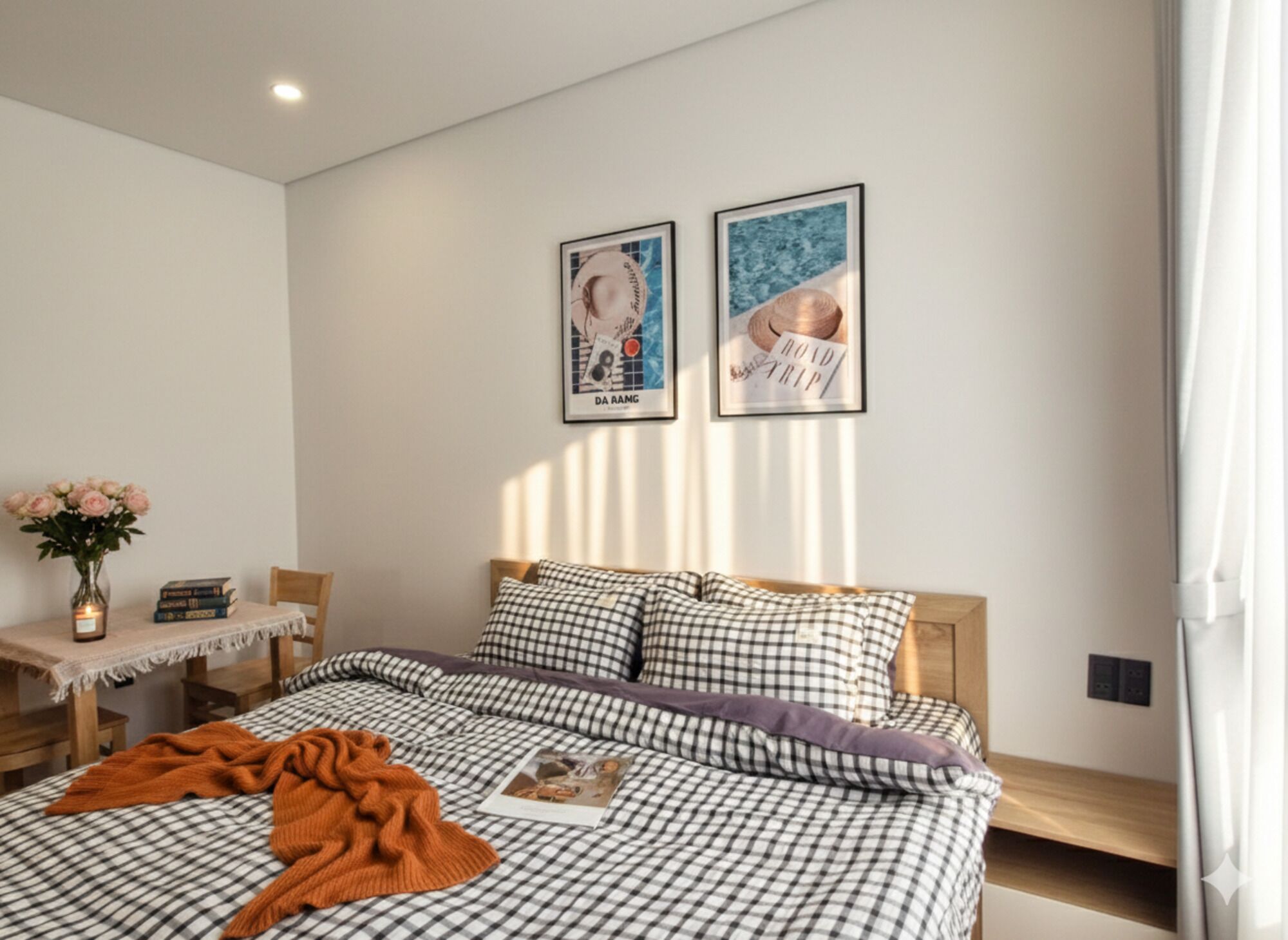 A bedroom with a checkered bedspread, a bedside table with a vase of flowers, and two framed posters on the wall.