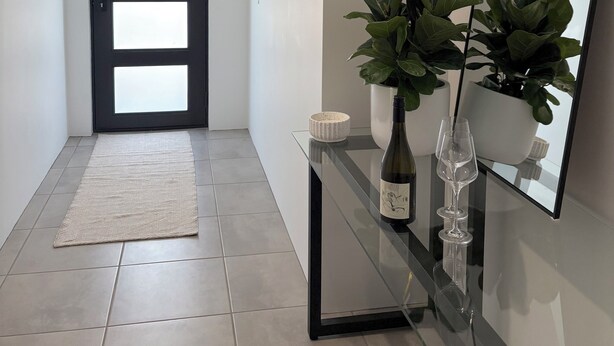 A modern hallway with a glass console table, a potted plant, a wine bottle, and a wine glass. - Innerbloom Stay Busselton - Guest House (West Busselton)