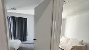 A modern hotel room with a bed, a sofa, and a large window with blinds. - Innerbloom Stay Busselton - Guest House (West Busselton)