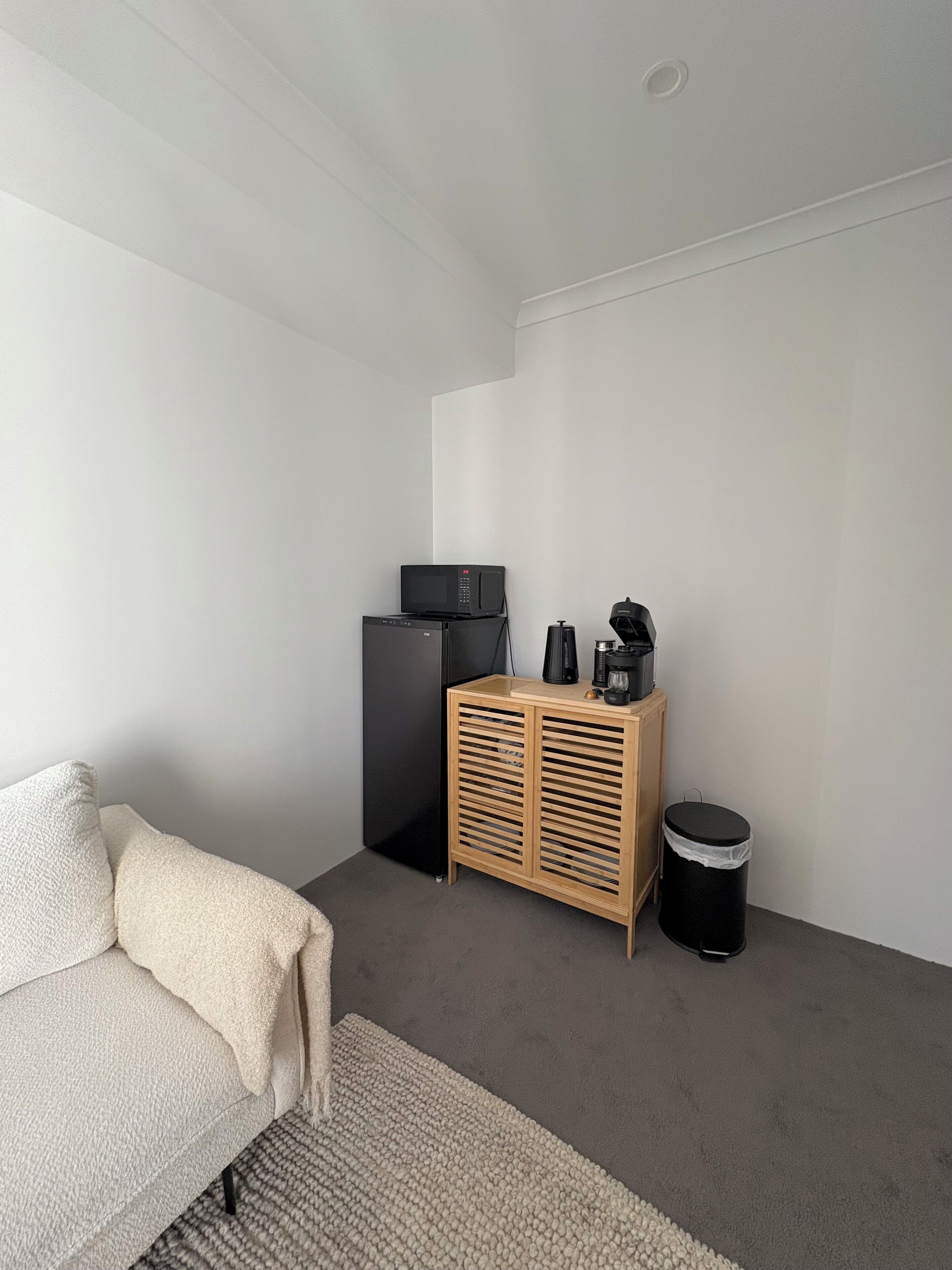 Une pièce au décor minimaliste, avec un canapé, un petit meuble, une poubelle et un four à micro-ondes.
