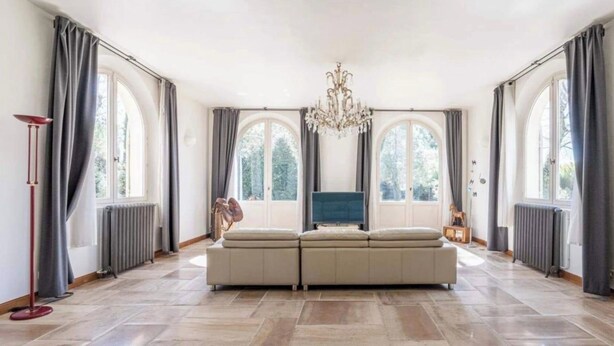 Ein geräumiges Wohnzimmer mit einer großen Eckcouch, einem Chandelier und großen Fenstern mit Vorhängen.