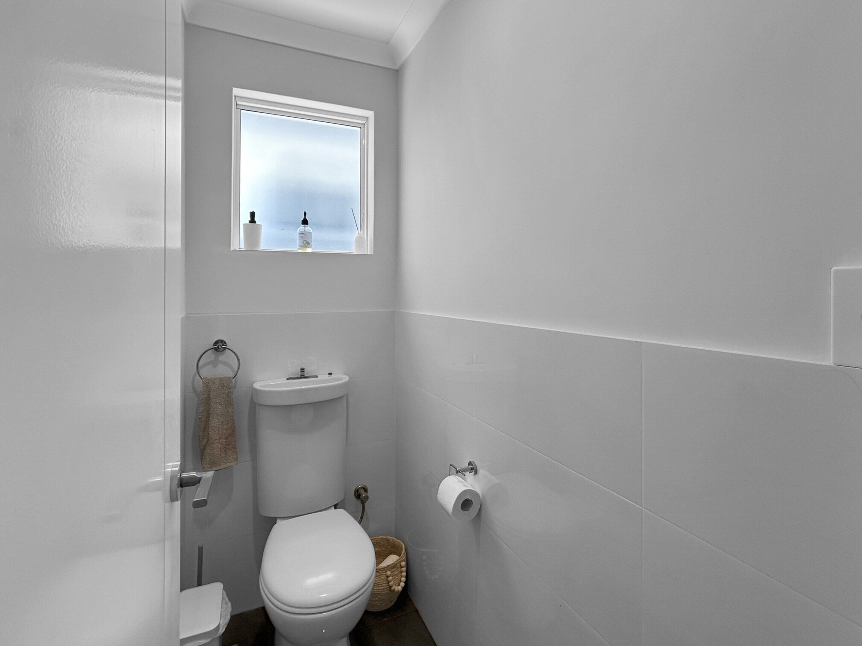 Une petite salle de bain blanche, avec des toilettes, un lavabo et une fenêtre.