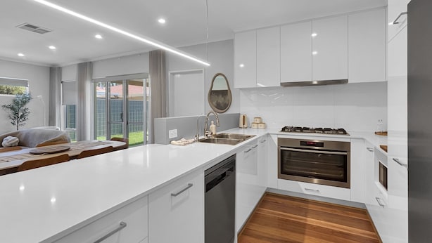 Una cocina moderna con armarios blancos, una isla central, electrodomésticos de acero inoxidable y vistas al exterior.