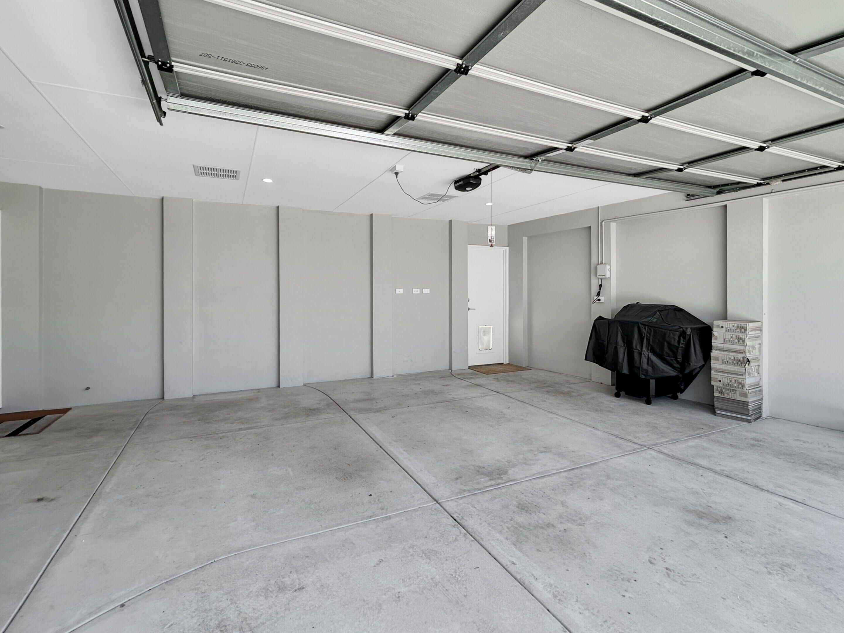 A spacious, empty room with a high ceiling, concrete flooring, and a door leading to another area.